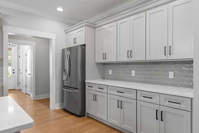 kitchen featuring light wood-style floors, decorative backsplash, light stone counters, crown molding, and stainless steel refrigerator with ice dispenser