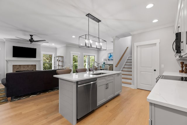 kitchen featuring an island with sink, hanging light fixtures, sink, dishwasher, and light hardwood / wood-style floors