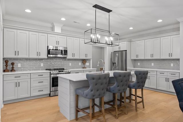 kitchen featuring stainless steel appliances, backsplash, light countertops, crown molding, and a center island with sink