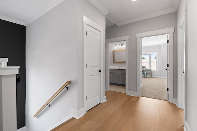 hallway featuring ornamental molding, a sink, an upstairs landing, light wood-style floors, and baseboards