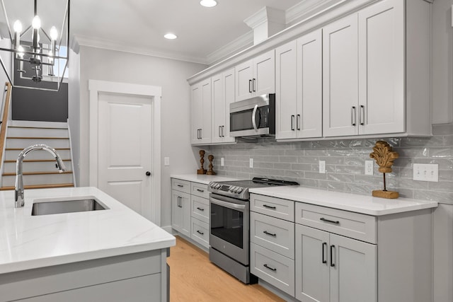 kitchen featuring light wood finished floors, stainless steel appliances, ornamental molding, a sink, and tasteful backsplash