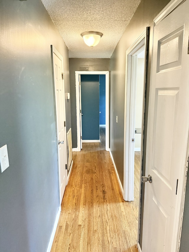 corridor with a textured ceiling and light wood-type flooring