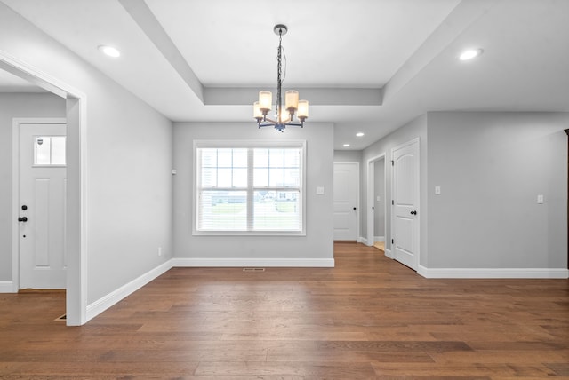 unfurnished dining area with a notable chandelier, a raised ceiling, and dark wood-type flooring