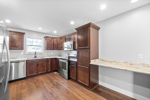 kitchen with appliances with stainless steel finishes, light stone countertops, dark hardwood / wood-style flooring, dark brown cabinetry, and sink