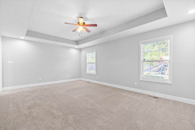 carpeted spare room with a raised ceiling and ceiling fan