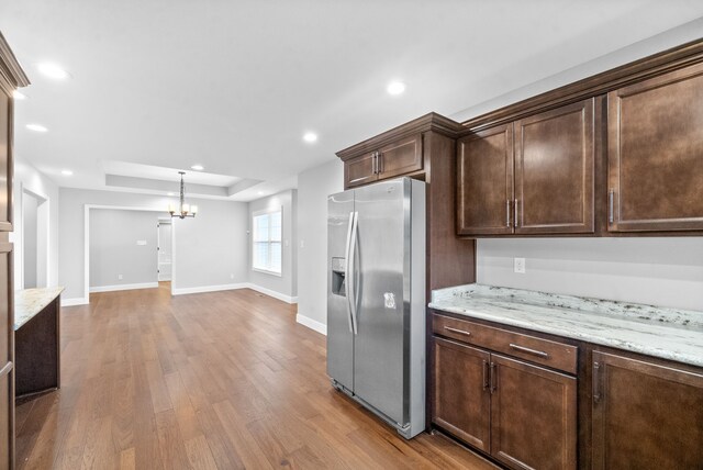 kitchen with stainless steel fridge, light stone countertops, dark brown cabinets, an inviting chandelier, and light hardwood / wood-style flooring