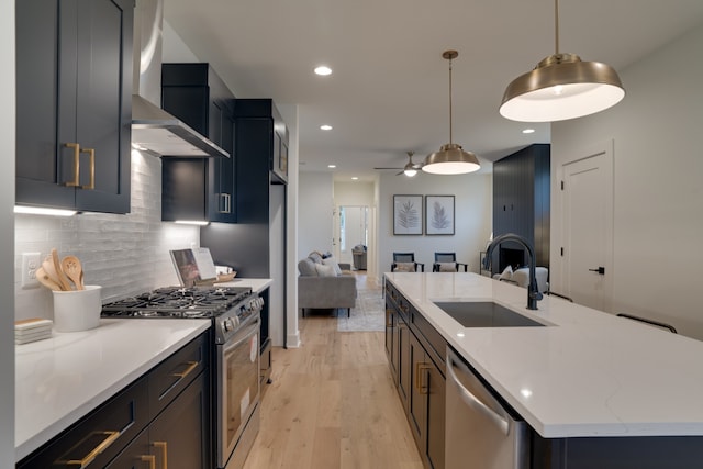 kitchen with pendant lighting, a kitchen island with sink, sink, light hardwood / wood-style flooring, and appliances with stainless steel finishes