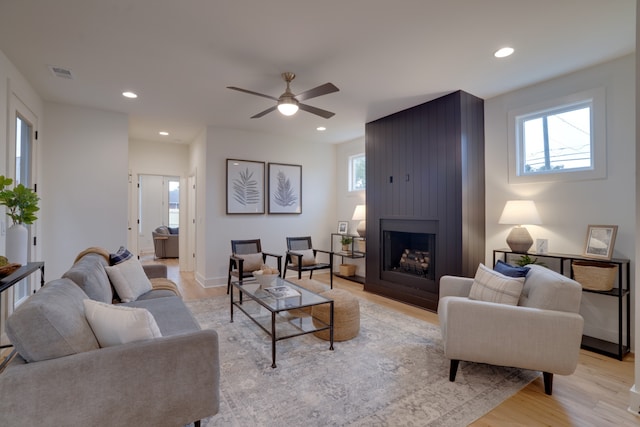 living room featuring light hardwood / wood-style flooring, ceiling fan, and a fireplace