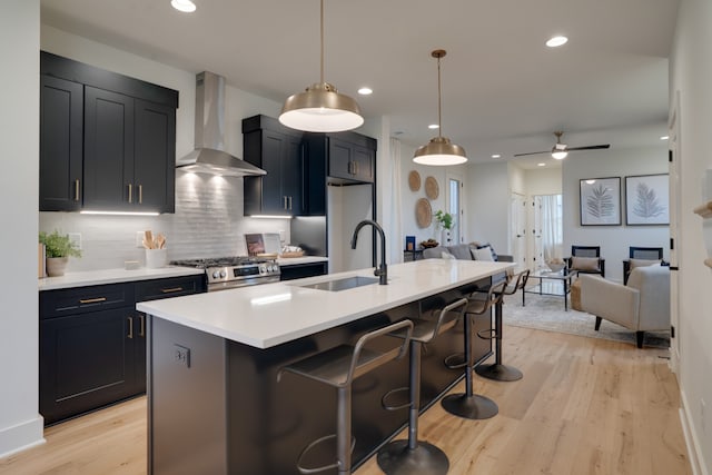 kitchen featuring wall chimney exhaust hood, a center island with sink, pendant lighting, and sink