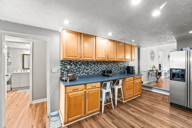 kitchen with light wood-type flooring, a textured ceiling, sink, backsplash, and stainless steel fridge