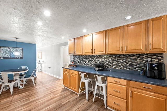 kitchen with light hardwood / wood-style flooring, decorative backsplash, a textured ceiling, and decorative light fixtures