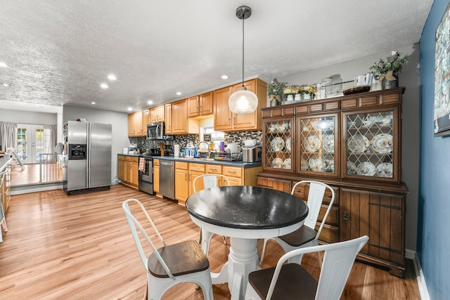 kitchen with pendant lighting, a textured ceiling, light hardwood / wood-style flooring, appliances with stainless steel finishes, and decorative backsplash