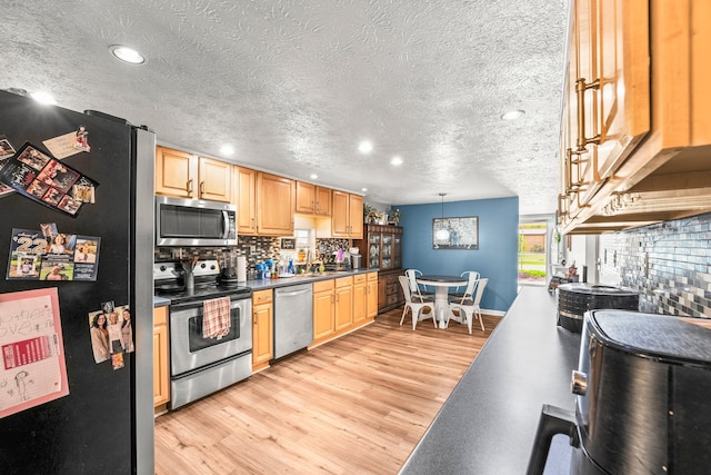 kitchen featuring light hardwood / wood-style floors, a textured ceiling, tasteful backsplash, hanging light fixtures, and appliances with stainless steel finishes