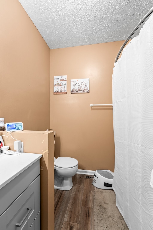 bathroom with a textured ceiling, hardwood / wood-style flooring, walk in shower, vanity, and toilet