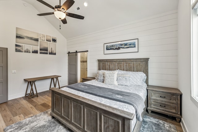 bedroom featuring ceiling fan, vaulted ceiling, hardwood / wood-style flooring, and a barn door