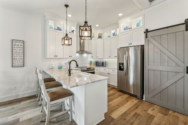 kitchen featuring light stone counters, a barn door, pendant lighting, stainless steel appliances, and light wood-type flooring