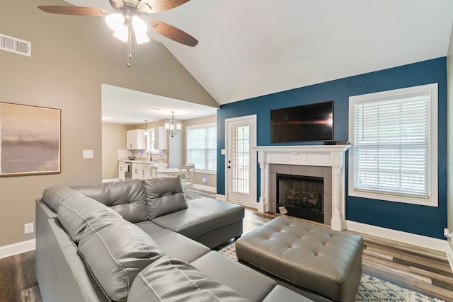 living room with hardwood / wood-style flooring, sink, ceiling fan with notable chandelier, a fireplace, and high vaulted ceiling