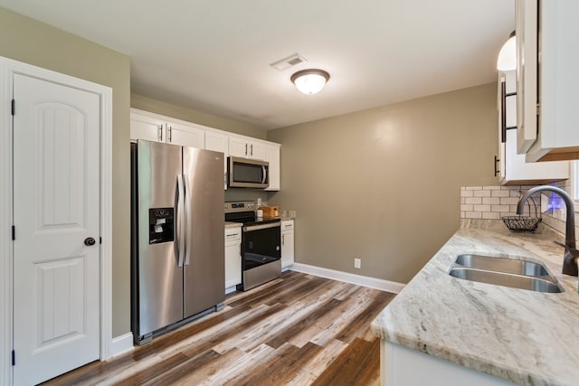 kitchen featuring appliances with stainless steel finishes, light stone counters, white cabinets, wood-type flooring, and sink