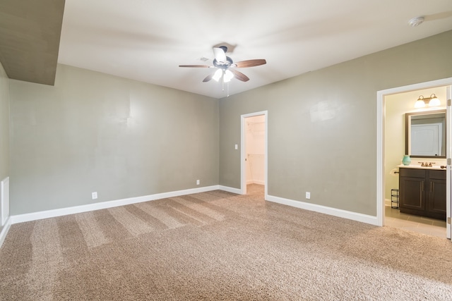 unfurnished bedroom with a closet, light carpet, a walk in closet, ensuite bathroom, and ceiling fan