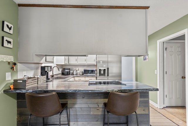 kitchen with appliances with stainless steel finishes, a kitchen breakfast bar, white cabinetry, kitchen peninsula, and sink