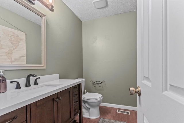 bathroom with wood-type flooring, a textured ceiling, vanity, and toilet