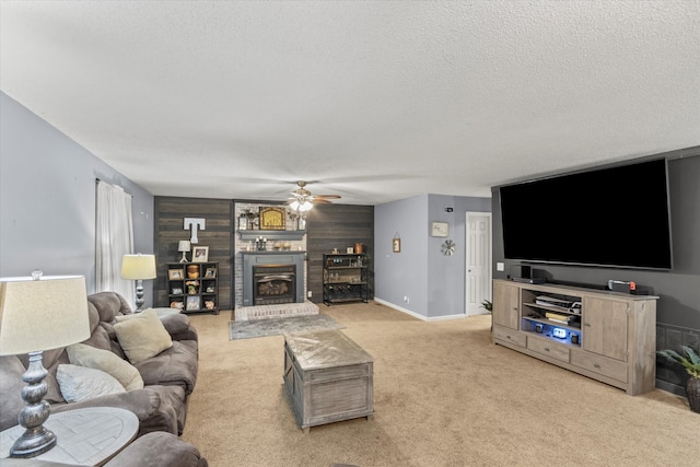 carpeted living room featuring ceiling fan, a textured ceiling, a fireplace, and wood walls