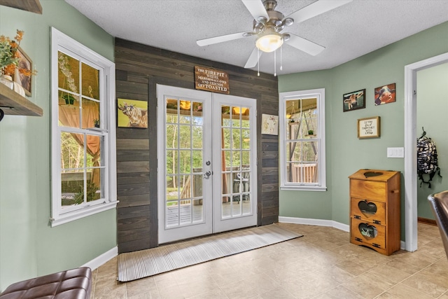 doorway to outside featuring wooden walls, ceiling fan, french doors, and a textured ceiling