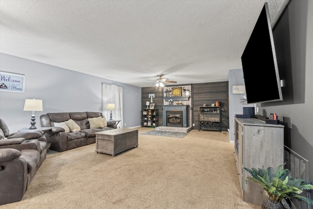 carpeted living room featuring a large fireplace, ceiling fan, and a textured ceiling