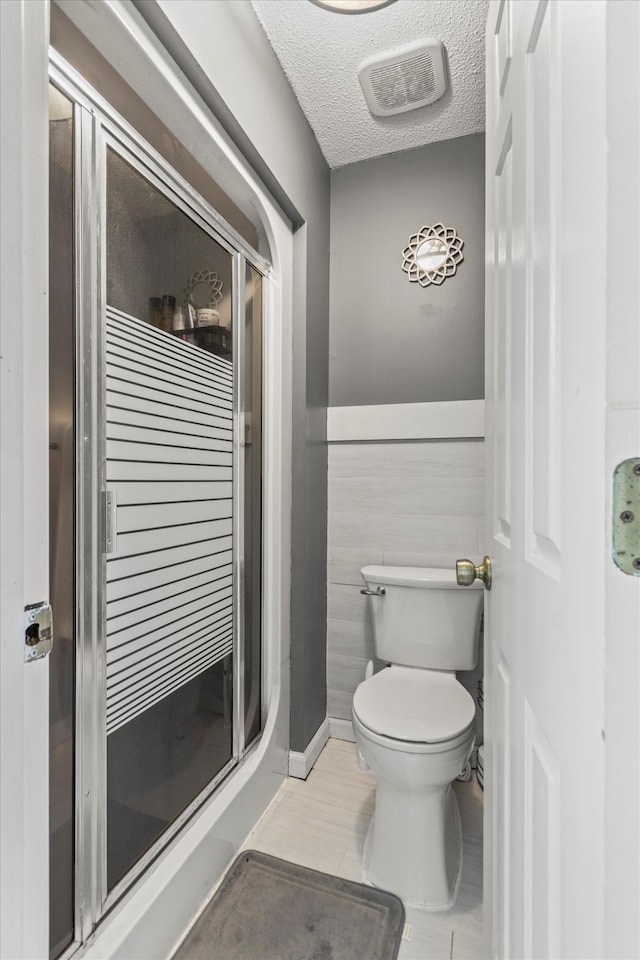 bathroom with tile walls, a textured ceiling, tile patterned floors, a shower with shower door, and toilet