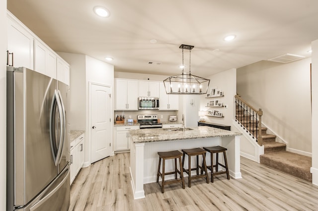 kitchen featuring sink, white cabinetry, a center island with sink, appliances with stainless steel finishes, and decorative light fixtures