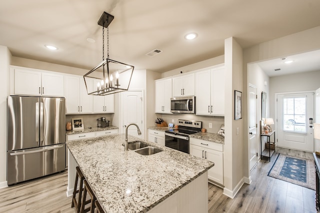 kitchen featuring appliances with stainless steel finishes, light hardwood / wood-style floors, an island with sink, white cabinets, and sink