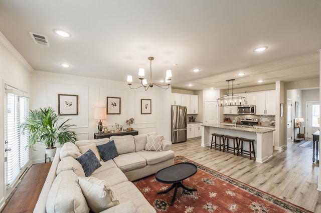 living room with light wood-type flooring, ornamental molding, an inviting chandelier, and sink