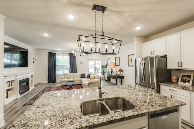 kitchen featuring wood-type flooring, sink, white cabinetry, hanging light fixtures, and stainless steel appliances