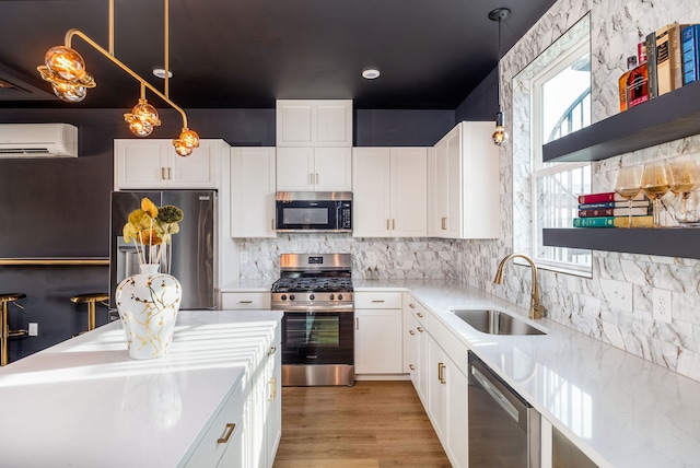 kitchen featuring appliances with stainless steel finishes, white cabinetry, an AC wall unit, decorative light fixtures, and sink