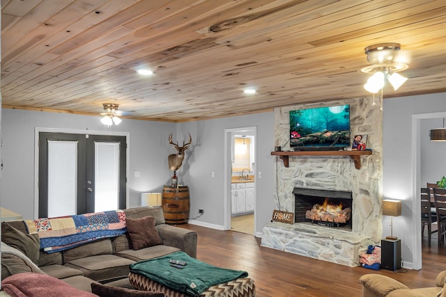 living room with wood ceiling, wood-type flooring, sink, a stone fireplace, and ceiling fan