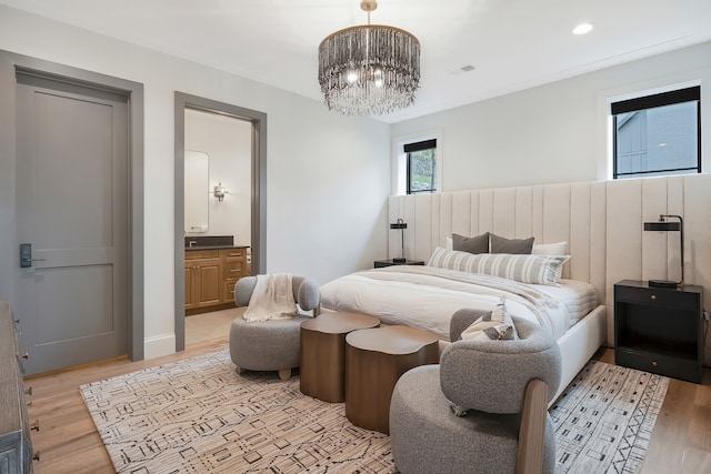 bedroom with light hardwood / wood-style floors, an inviting chandelier, and ensuite bath