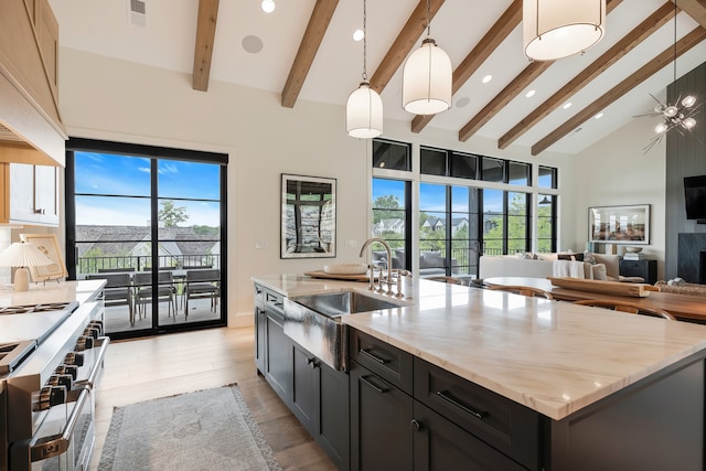 kitchen featuring an island with sink, hanging light fixtures, beam ceiling, sink, and high vaulted ceiling