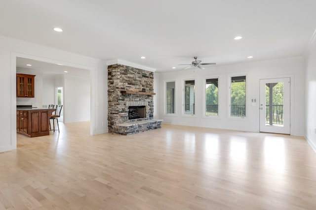 unfurnished living room featuring ornamental molding, light wood-type flooring, ceiling fan, and a stone fireplace