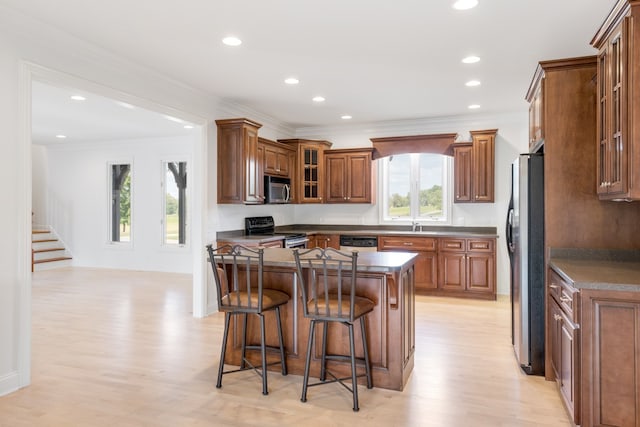 kitchen with appliances with stainless steel finishes, light wood-type flooring, a center island, and ornamental molding