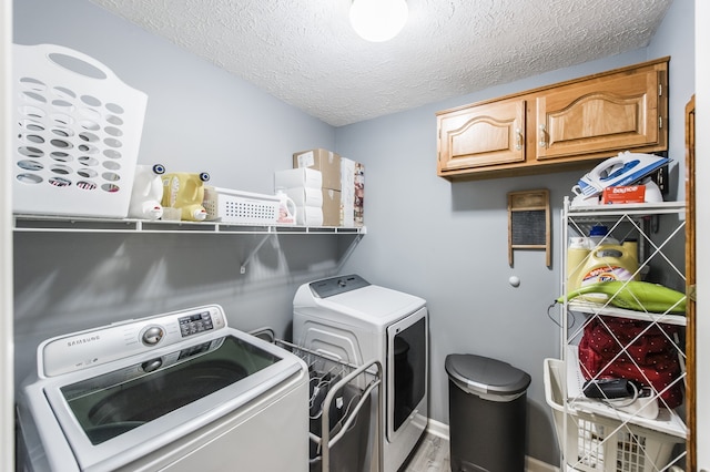 laundry room featuring a textured ceiling, washer and clothes dryer, light hardwood / wood-style floors, and cabinets