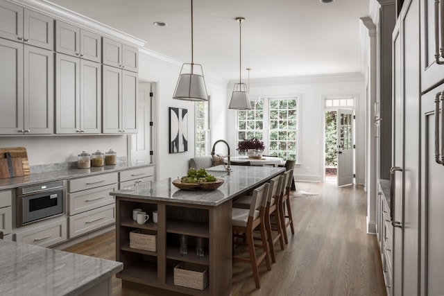 kitchen with decorative light fixtures, a kitchen bar, light stone countertops, and an island with sink