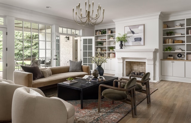 living room with hardwood / wood-style floors, built in shelves, crown molding, and a chandelier