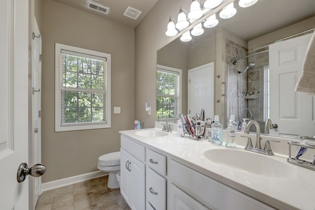 bathroom with a tile shower, a wealth of natural light, toilet, and vanity