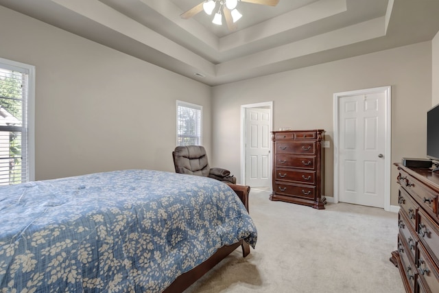 bedroom with light carpet, ceiling fan, and a tray ceiling