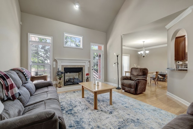 living room featuring high vaulted ceiling, light hardwood / wood-style floors, a tiled fireplace, a chandelier, and ornamental molding