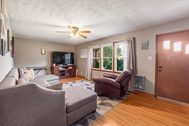 living room featuring ceiling fan, a textured ceiling, heating unit, and light wood-type flooring