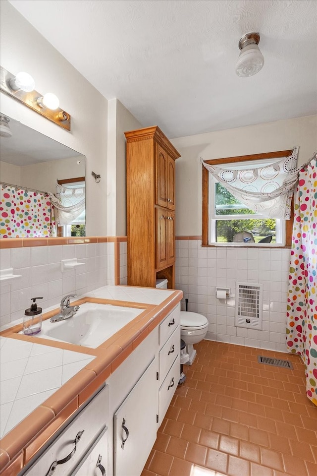 bathroom with a textured ceiling, toilet, tile walls, heating unit, and vanity