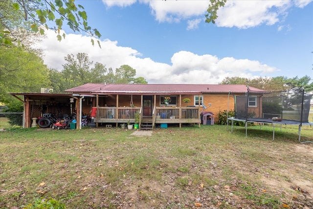 back of house with a deck, a lawn, and a trampoline