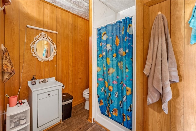 bathroom with wood-type flooring, a textured ceiling, toilet, walk in shower, and wooden walls