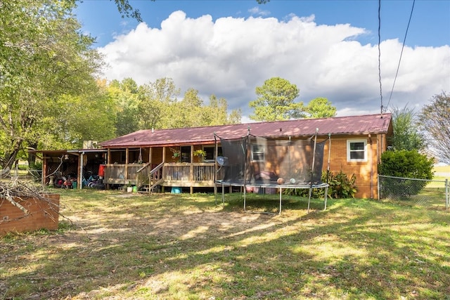 rear view of house featuring a deck, a yard, and a trampoline